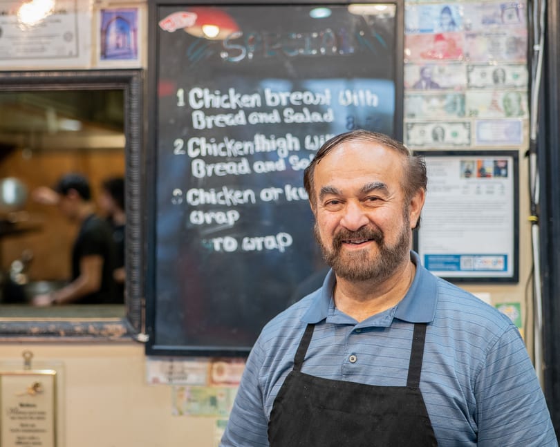 Smiling man in a blue polo and black apron stands in front of a specials board.
