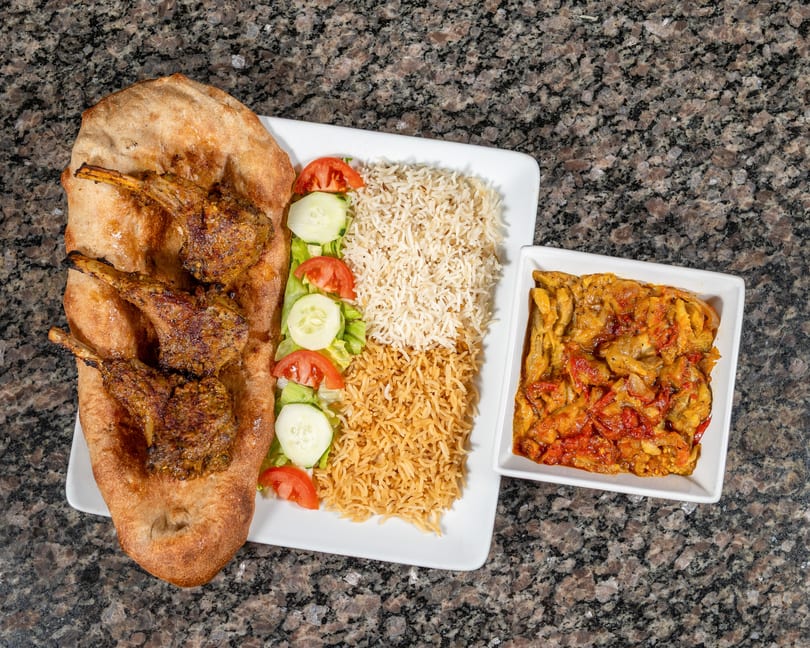 Grilled lamb chops on flatbread with rice, salad, and a side of stewed vegetables.