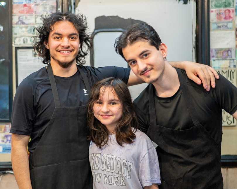 Two young men in black aprons and a young girl smiling at the camera.